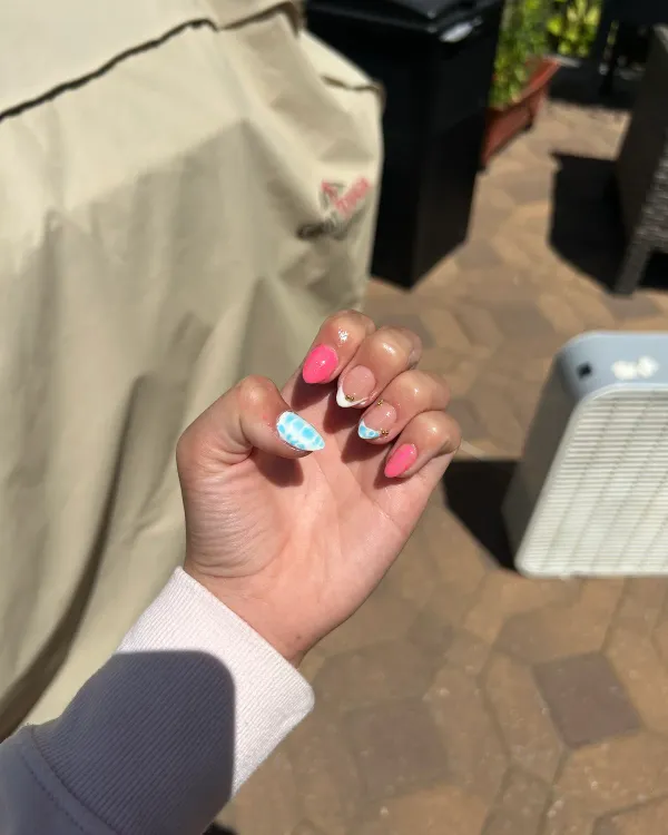 Almond-shaped nails with bright pink polish, blue-and-white patterns, French tips, and small gold accents.