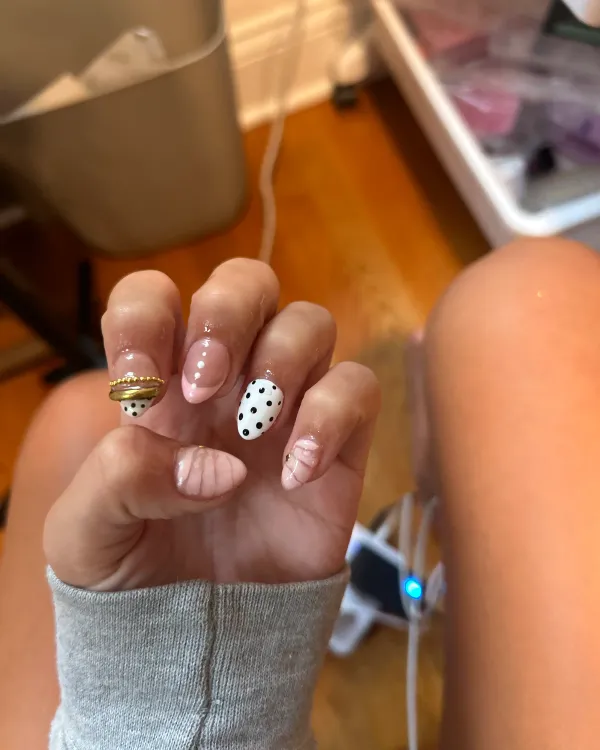 Pink and white almond-shaped nails with black polka dots, gold accents, and raised pink details.